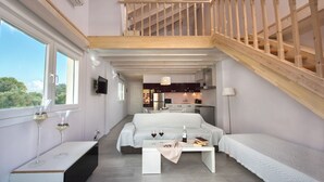 Un dormitorio tipo loft moderno con una escalera de madera, una zona de comedor y una cocina al fondo.