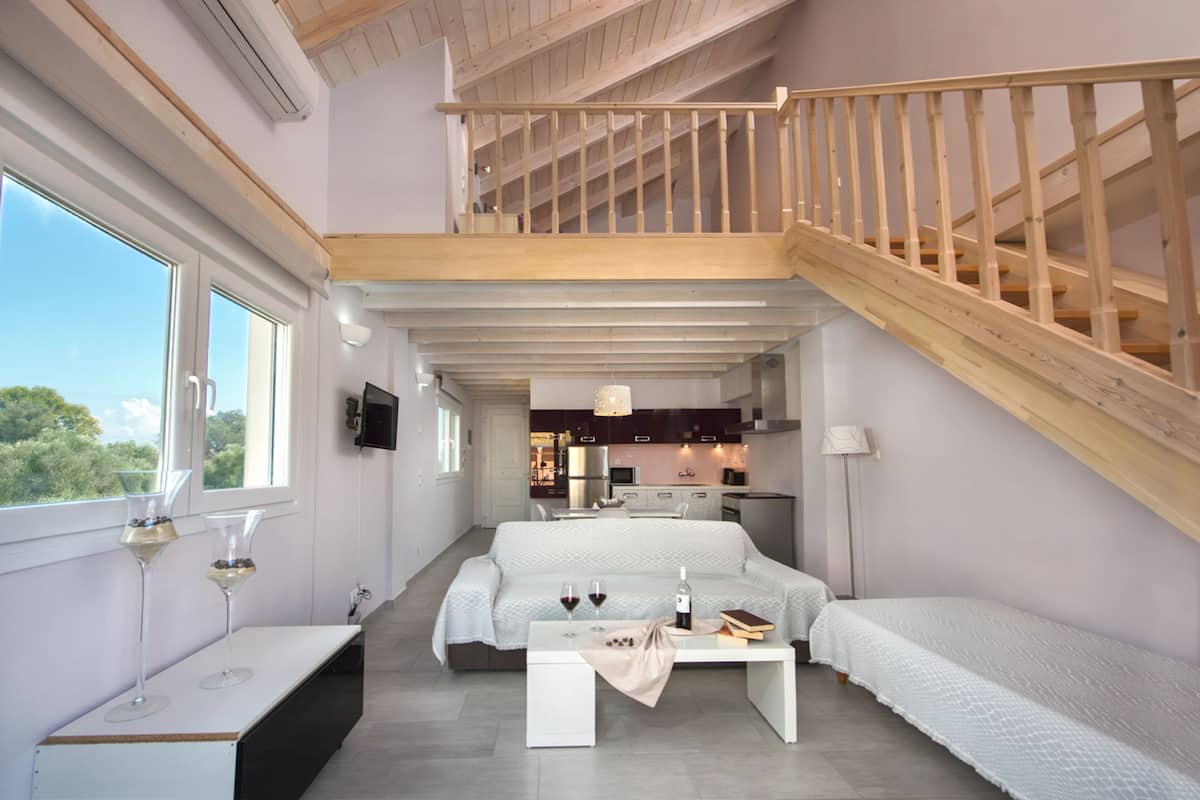 A modern loft bedroom with a wooden staircase, a dining area, and a kitchen in the background.