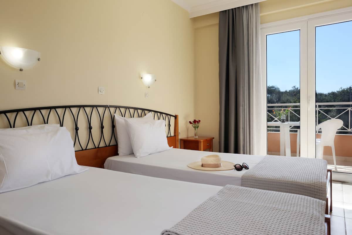 A hotel room with two beds, a balcony with a view, and a small table with a vase of flowers.