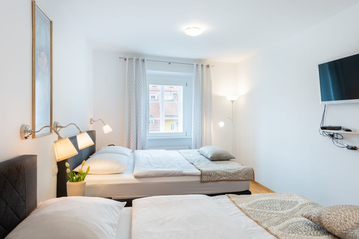 Une chambre d’hôtel avec deux lits, une fenêtre avec des rideaux, un téléviseur fixé au mur et une table de chevet avec une lampe.