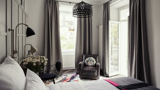 Een slaapkamer met een bed, een stoel, een lamp en een raam met gordijnen.