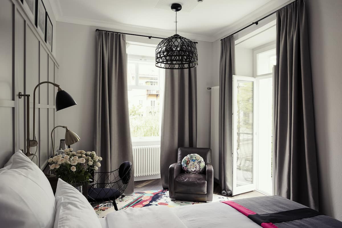 Une chambre à coucher avec un lit, une chaise, une lampe et une fenêtre avec des rideaux.