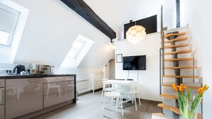 Een moderne keuken met een eethoek, een aan de muur bevestigde televisie en een houten trap.