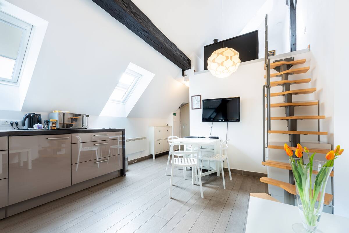 Une cuisine moderne avec un coin repas, un téléviseur fixé au mur et une échelle en bois.