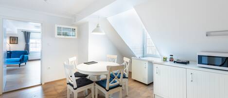 Une cuisine moderne avec des meubles blancs, une table à manger avec des chaises et un four à micro-ondes posé sur le plan de travail.
