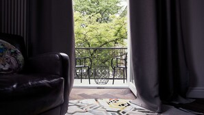 Een kamer met een zwarte leren bank, een kamerbreed tapijt met dessin, en een balkon met metalen stoelen en een hekwerk.