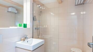 A modern bathroom with a glass shower enclosure, a white sink, and a small stool.
