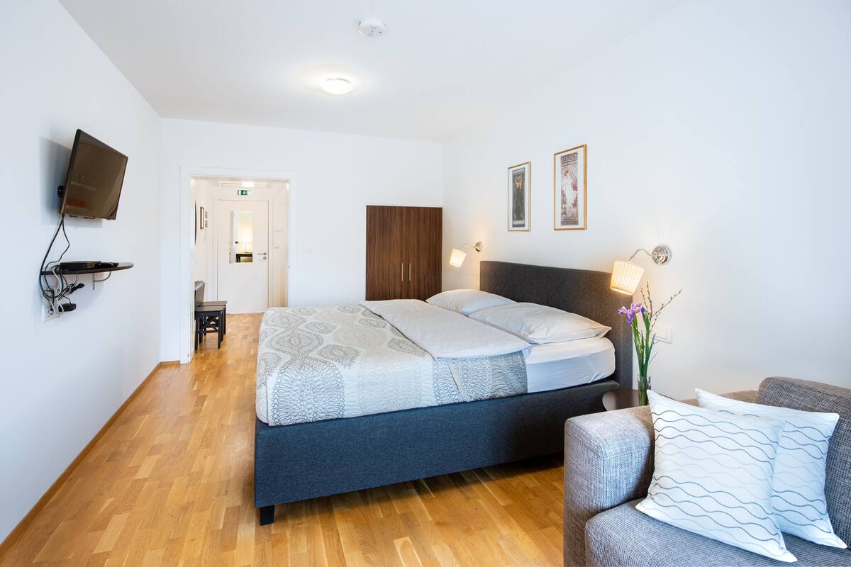 Une chambre d’hôtel moderne dotée d’un grand lit, d’un téléviseur à écran plat fixé au mur, d’une armoire en bois et d’un petit bureau avec une chaise.