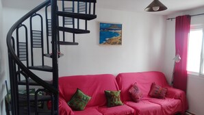A room with a red sofa, a spiral staircase, a painting on the wall, and a window with curtains. - LARGE TERRACE 60 M2, SEA VIEWS. Wi-Fi exclusive (Isleta del Moro)