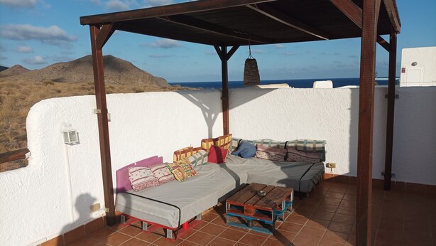 A covered outdoor seating area with a bed and a table, white walls, and a view of the sea. - LARGE TERRACE 60 M2, SEA VIEWS. Wi-Fi exclusive (Isleta del Moro)