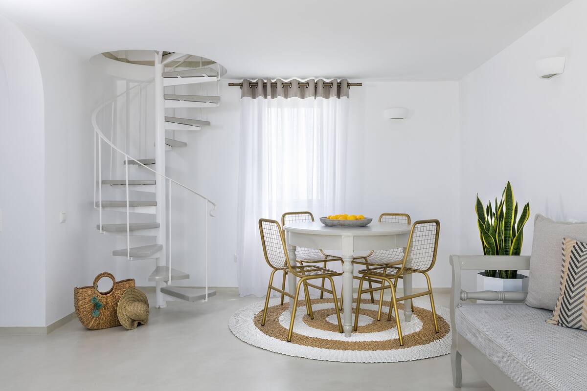 A modern interior with a spiral staircase, a dining area with a round table and chairs, a sofa with a plant, and a woven rug.
