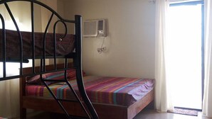 Quarto de dormitório com beliches, ventilador de teto, ar condicionado e janela com cortinas.