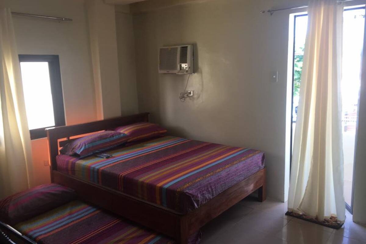 Una habitación con una cama, un banco y una ventana con cortinas.