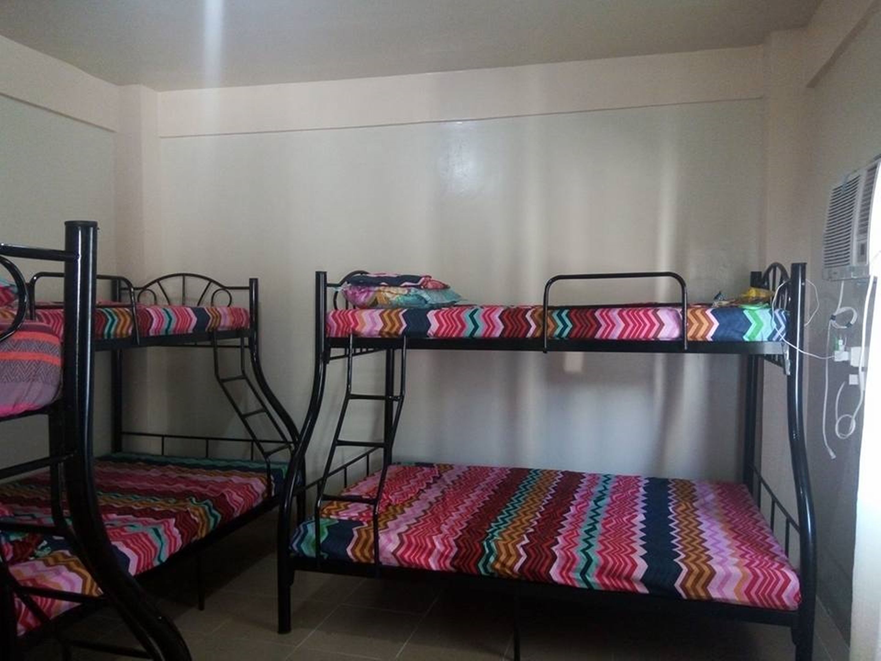 Bunk beds with colorful bedding in a room with white walls and a tiled floor.