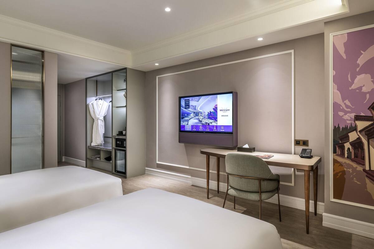 Una habitación de hotel con cama, escritorio, silla, televisor y armario.