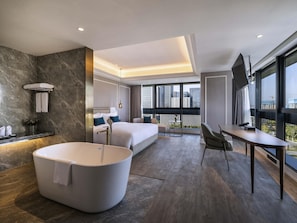 Una habitación de hotel moderna con una bañera grande, cama con vistas, escritorio y balcón con vistas a la ciudad.