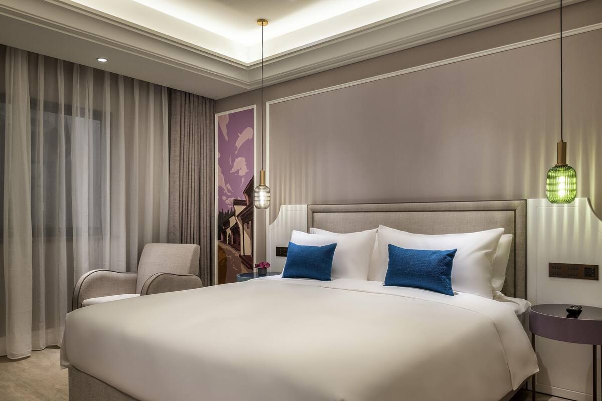 Una habitación de hotel moderna con una cama grande, una silla, una mesita de noche y una lámpara de pared.