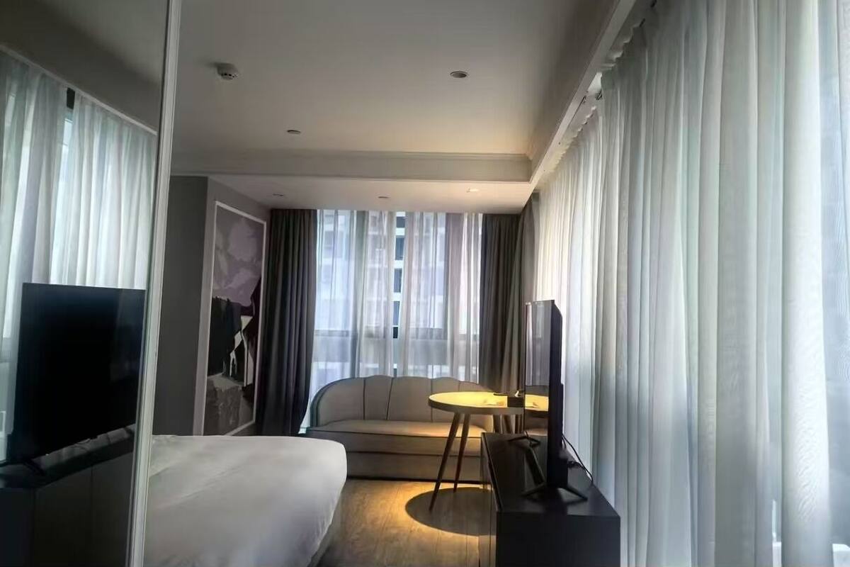 Una habitación de hotel con cama, televisor, sofá, una mesita y cortinas.