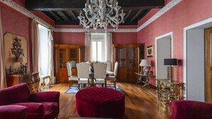 Een kamer met een kroonluchter, rode fauteuils, een eettafel en een rode poef.