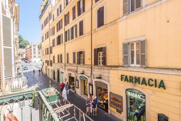 A street view with a pharmacy named 'FARMACIA' on the right, a pharmacy named 'CAESAR' across the street, and a building with a sign 'EMERGENZA' on the left.