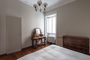 A bedroom with a bed, dresser, vanity with mirror, and a radiator.