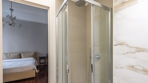 Een slaapkamer met een bed, een nachtkastje, een kroonluchter en een douche met glazen wanden.