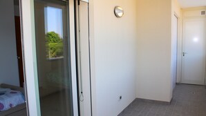 Une pièce dotée d’une porte-fenêtre coulissante donnant sur un balcon, d’un mur blanc avec un interrupteur et d’une porte fermée au bout du couloir.