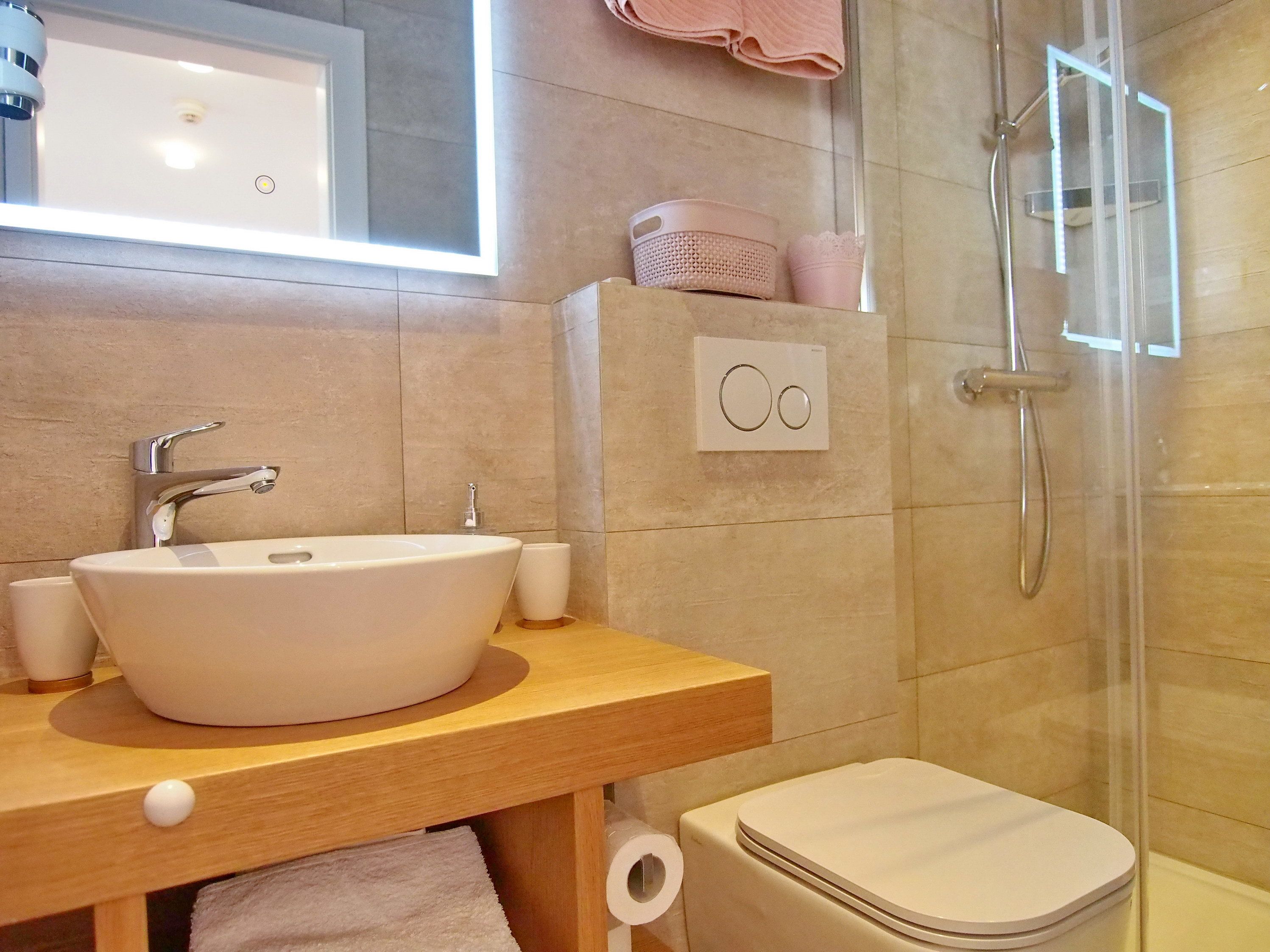 Ein Badezimmer mit weißem Waschbecken, einem Spiegel, einer Dusche und einer Toilette.