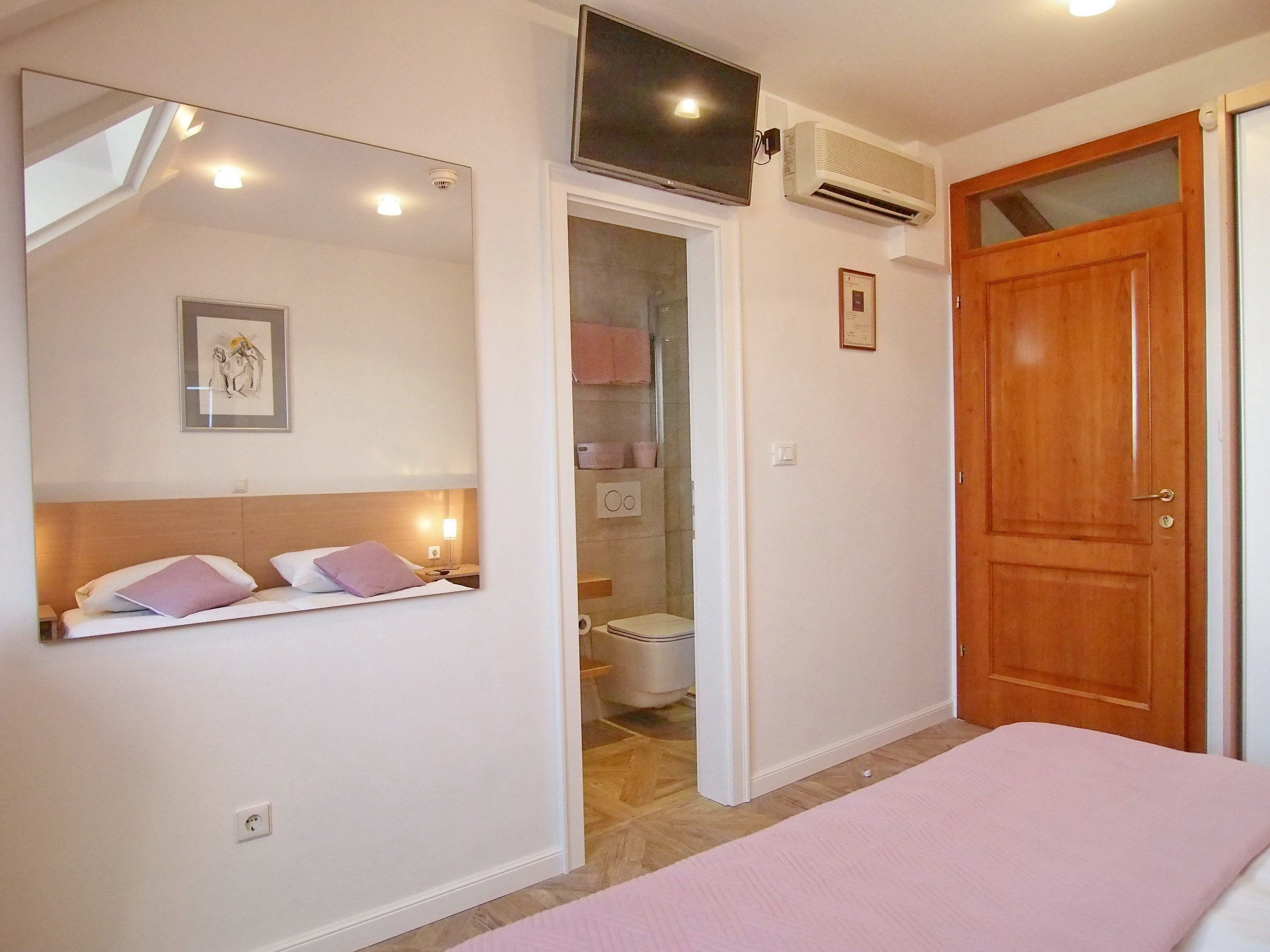 Une chambre à coucher avec un lit, un téléviseur fixé au mur, un appareil de climatisation et une porte en bois.