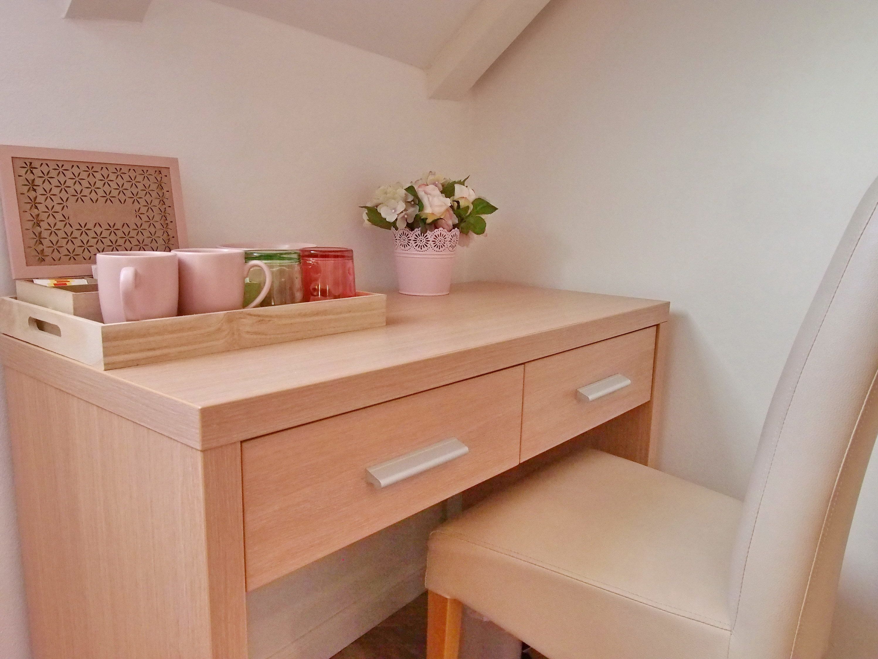 A wooden desk with drawers, a bench, and a potted plant with flowers.