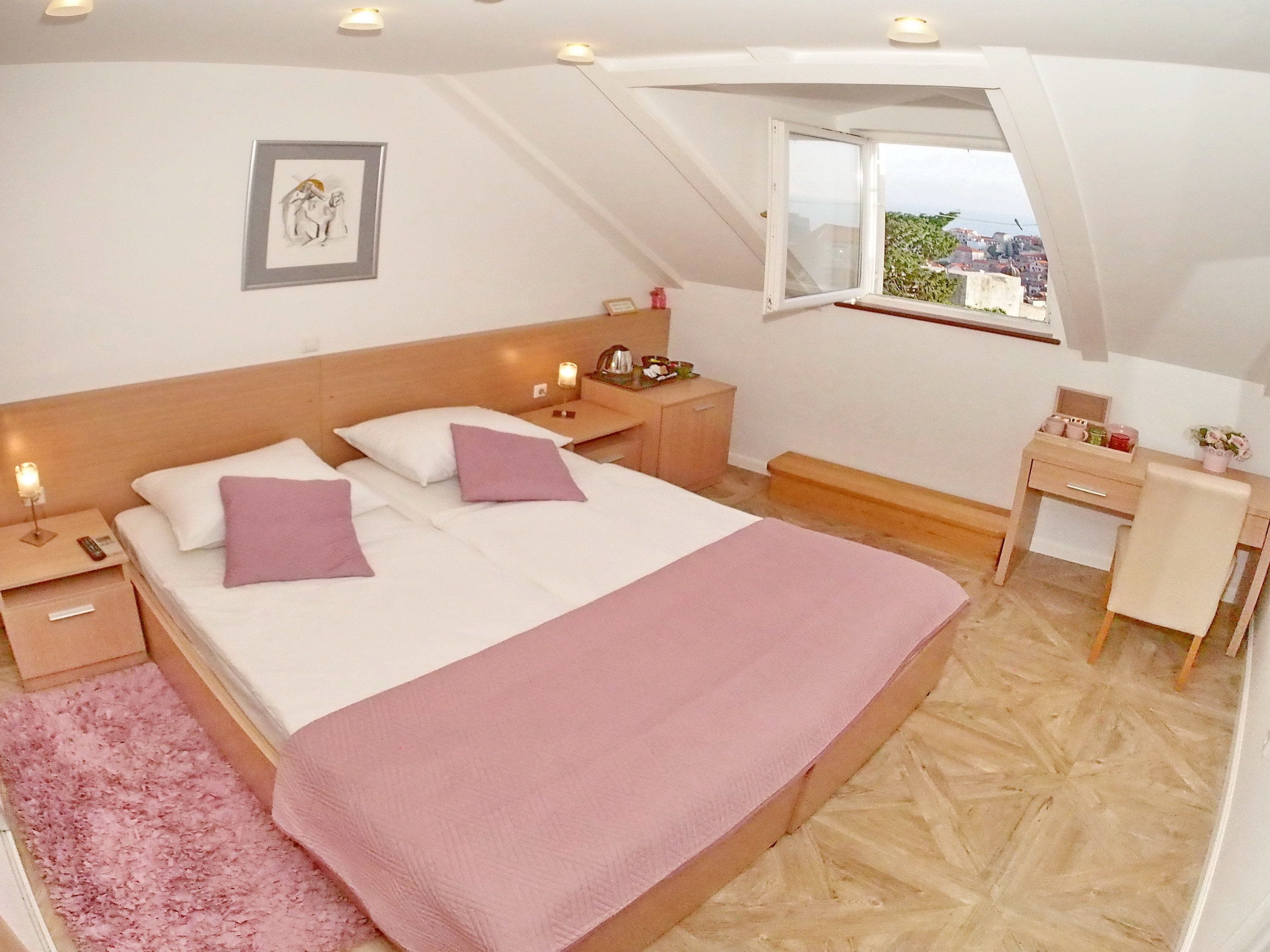 Une chambre à coucher avec un lit, des tables de chevet, un bureau et une fenêtre donnant sur un paysage agréable.