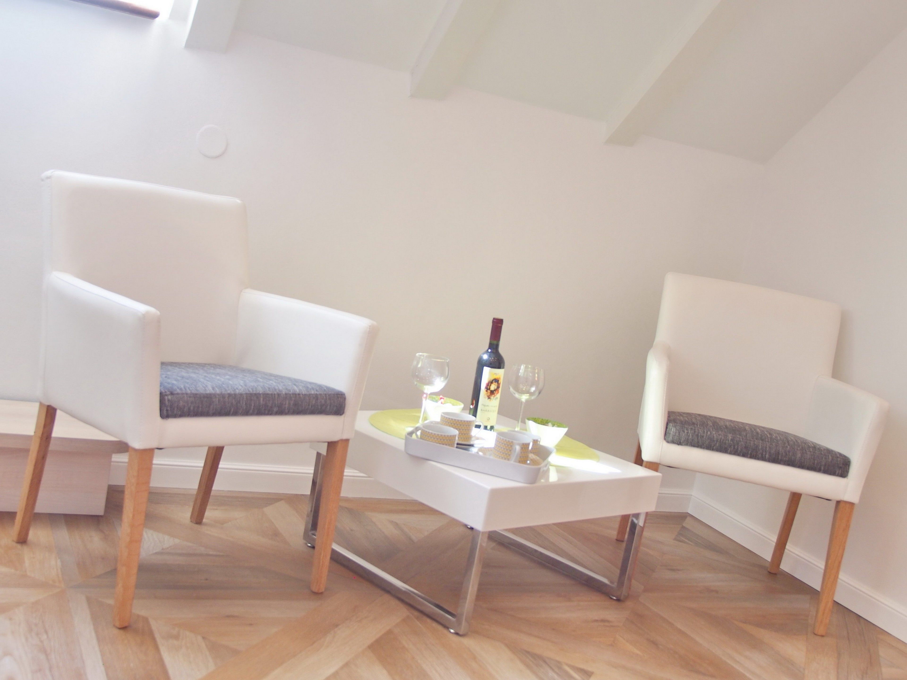 A modern room with two white armchairs, a small white table, and a bottle of wine.