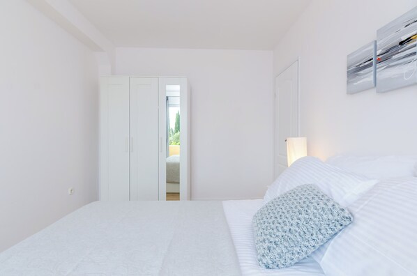 Quarto com cama, porta branca e vista para um jardim pela porta.