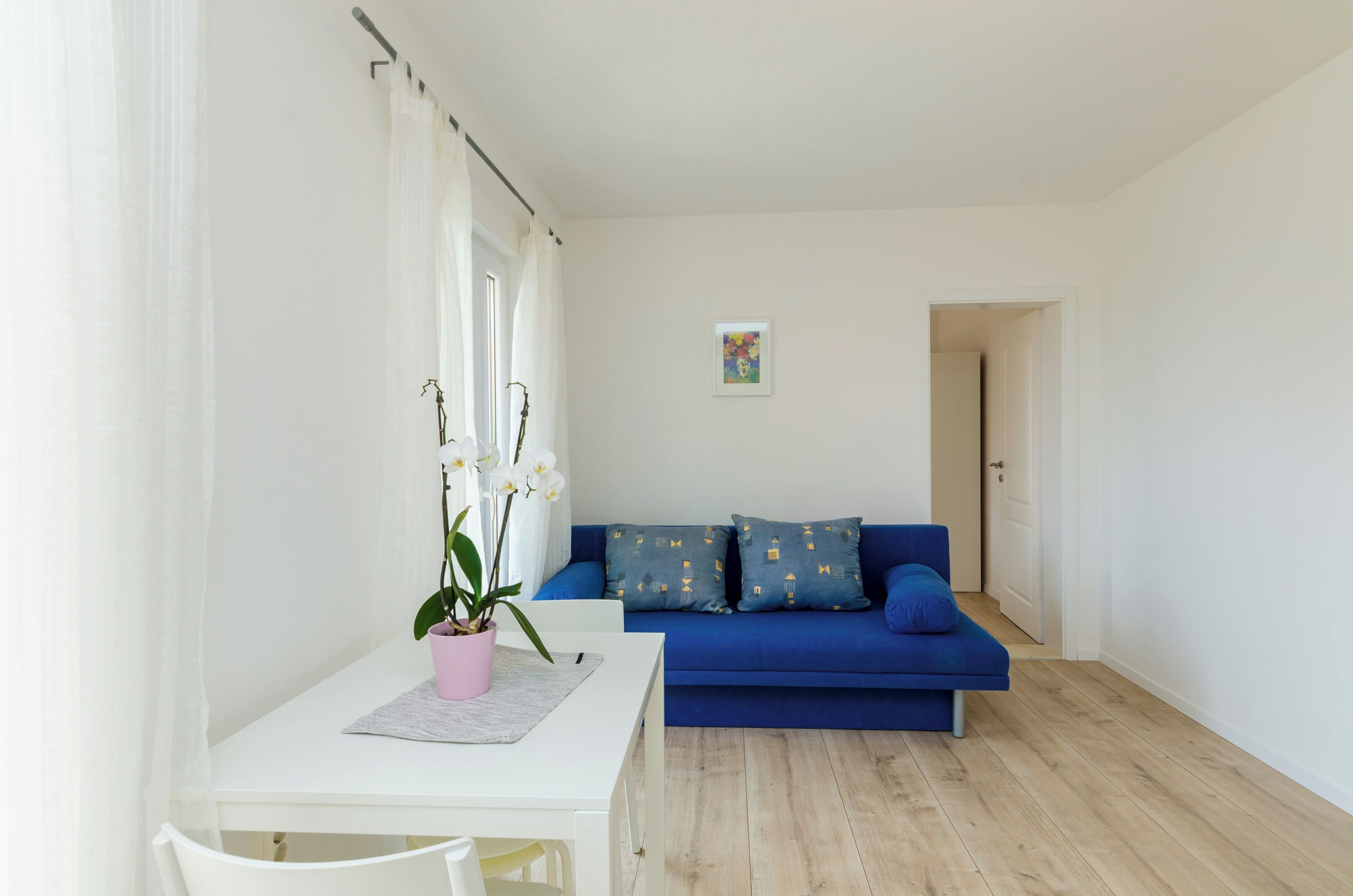 A living room with a white table, a blue sofa, and a potted orchid.