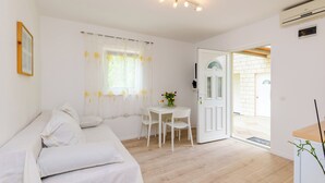 A room with a white sofa, a small table with a vase of flowers, and a door leading to an outdoor area. - Color Apartments (Zupa dubrovacka)