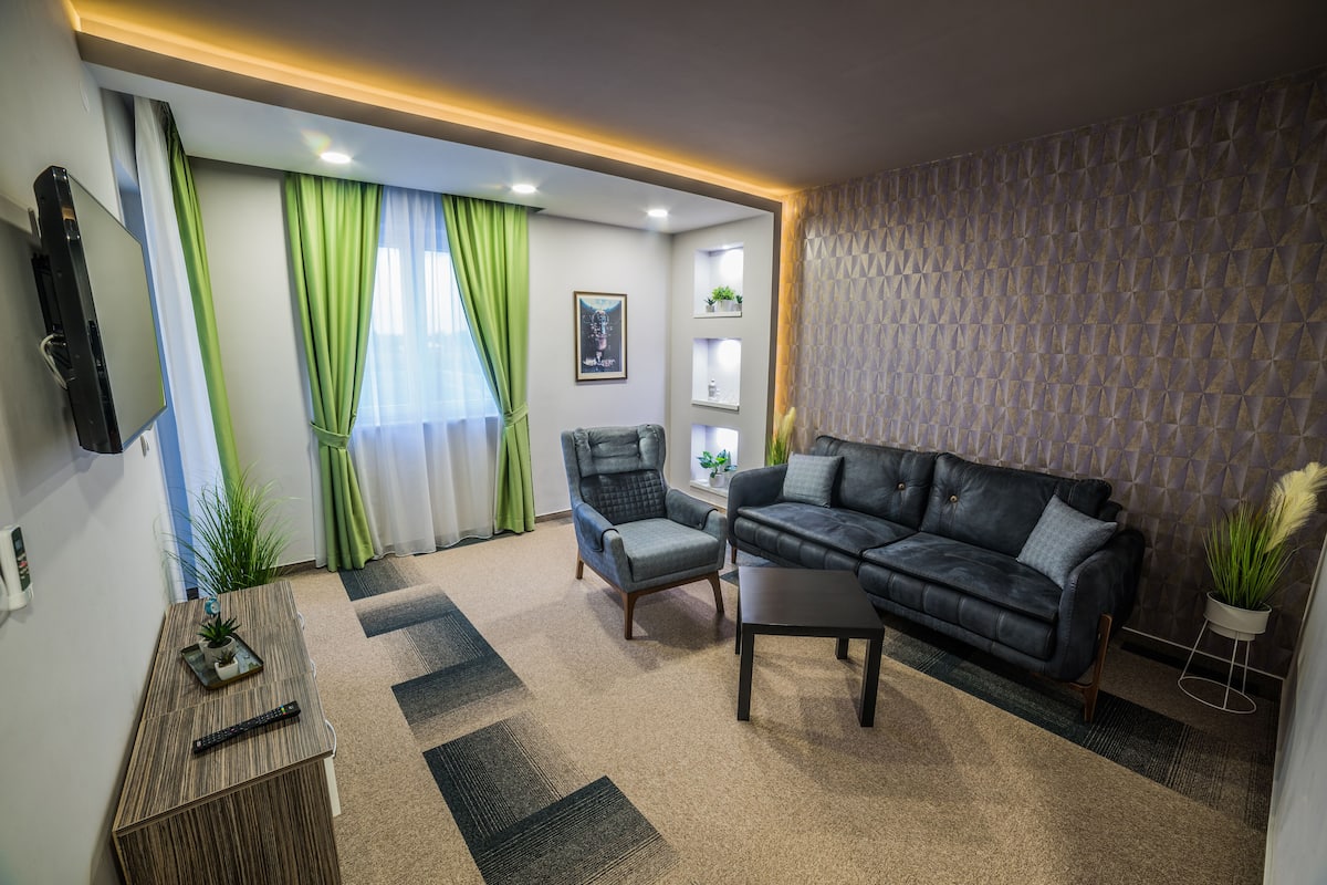 A modern living room with a sofa, armchair, and a flat-screen TV mounted on the wall.