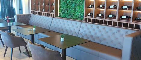Un interior de restaurante moderno con un banco largo, sillas acolchadas y una pared llena de botellas de vino.