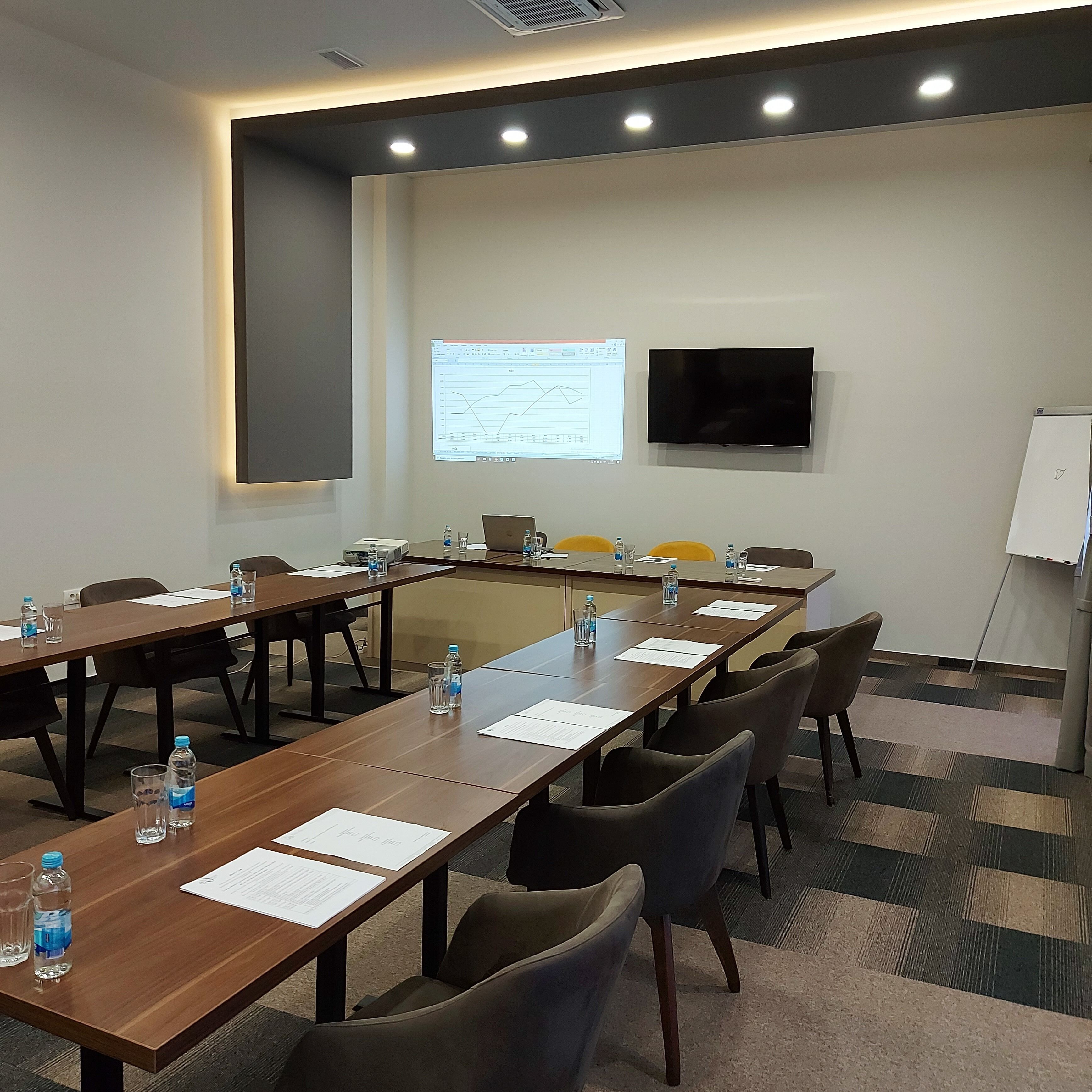 A conference room with long tables, chairs, a projector screen, and a flat-screen TV.