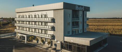 A modern hotel with a flat roof, multiple balconies, and a parking lot.
