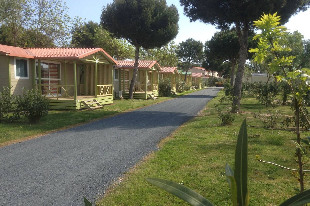 A row of single-story cabins with red roofs, a paved road, and surrounding greenery.