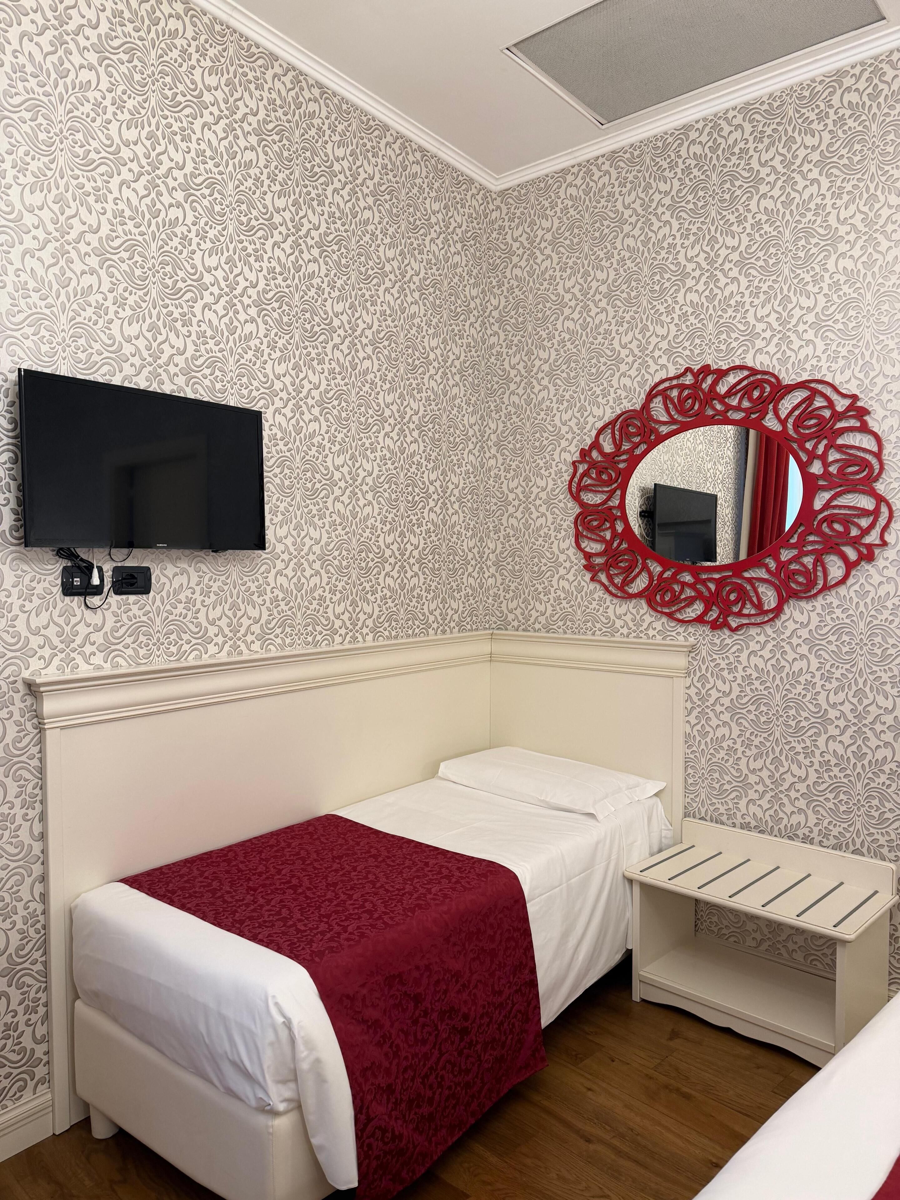 Un dormitorio con cama, televisor, espejo y mesita de noche.