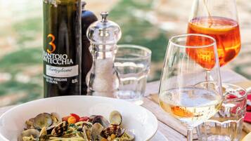 A table with a bowl of pasta, a wine bottle, glasses, and a salt shaker.