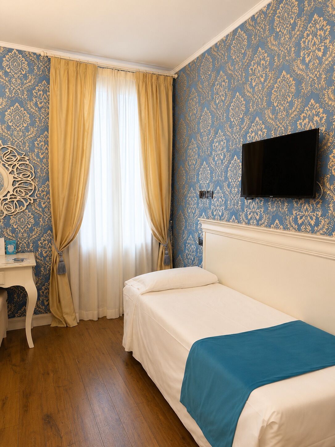 Una habitació d'hotel amb un llit, un escriptori, una televisió i una finestra amb cortines.