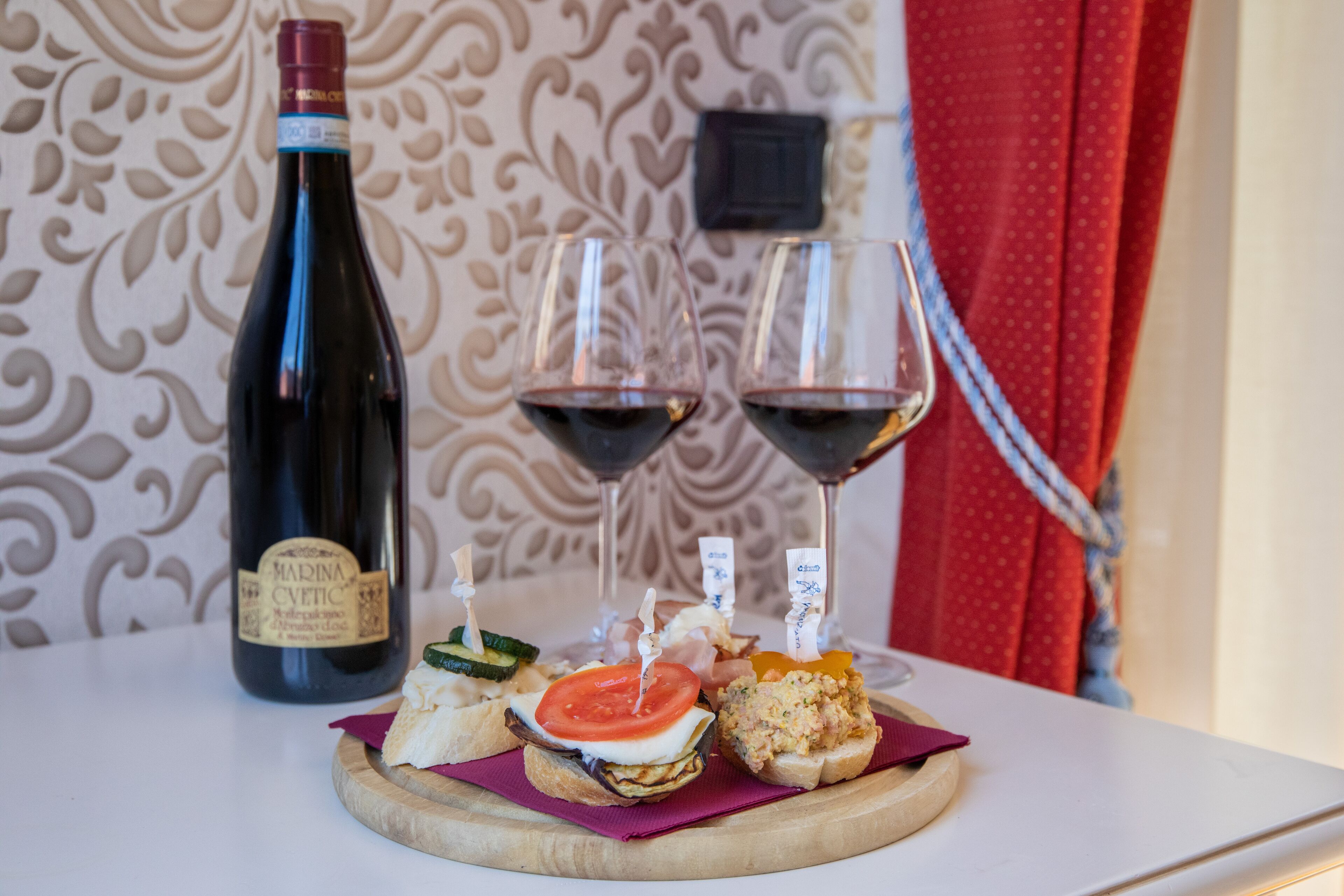 Une table avec une bouteille de vin, deux verres de vin rouge et une planche en bois sur laquelle sont disposés divers amuse-gueule.