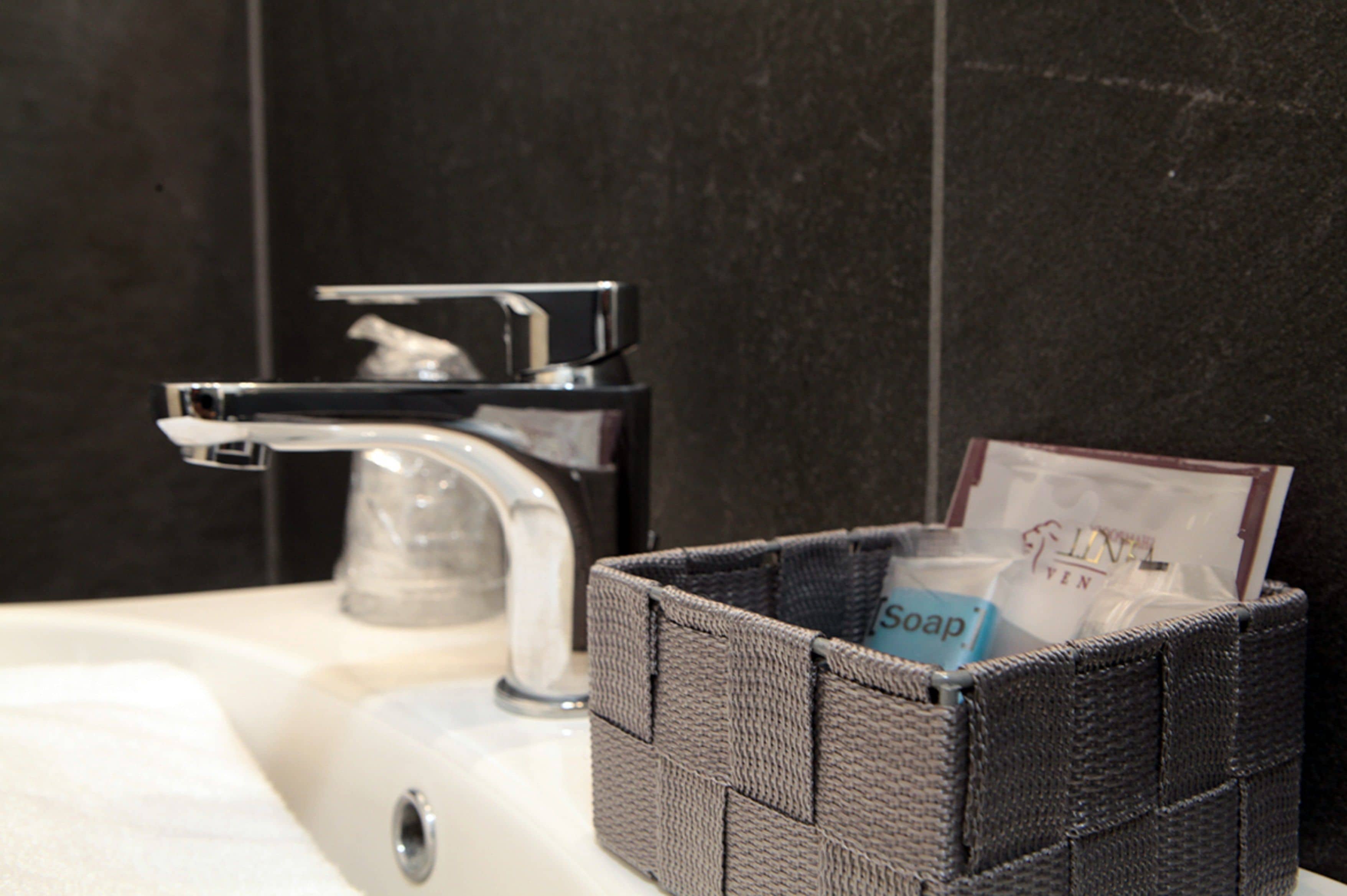 Un lavabo de salle de bain avec un robinet chromé et un distributeur de savon placé dans un panier tressé.