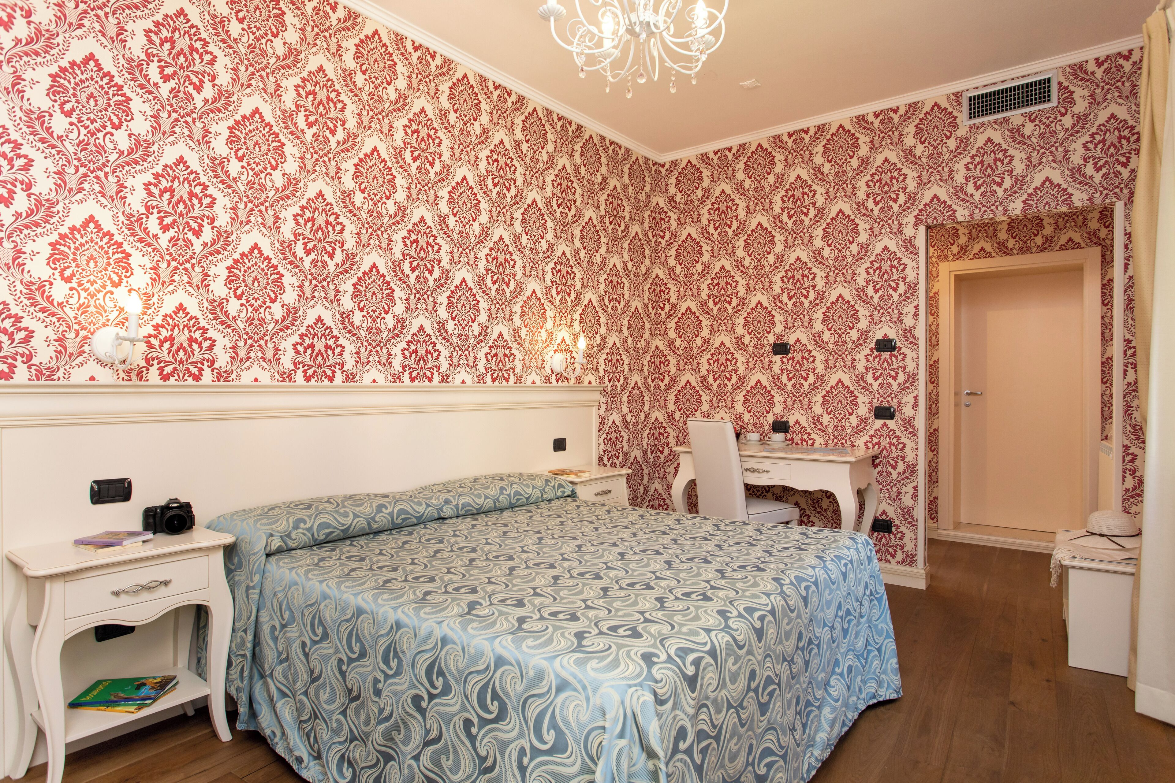 Una camera da letto con carta da parati fantasia, un letto con copriletto a motivi blu, una scrivania con sedia e un'armadio bianco.
