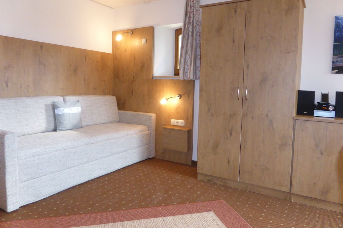 Een kamer met een bank, een houten garderobe en een bijzettafeltje met speakers.