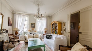 Een traditionele woonkamer met een groene salontafel, witte banken en een boekenkast.