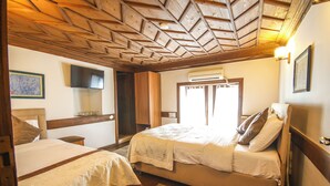 A room with two beds, wooden ceiling, and a flat-screen TV.