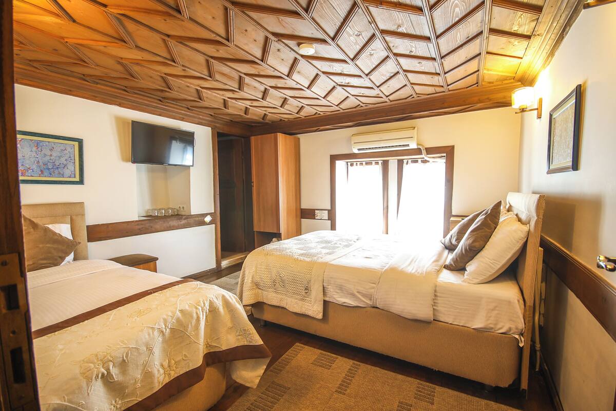 Une chambre avec deux lits, un plafond en bois et un téléviseur à écran plat.